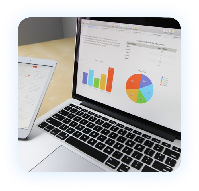 Laptop screen displaying charts and spreadsheet data next to a tablet showing a calendar on a table with a blurred background, framed in a light blue rounded square.