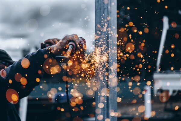 Close-up of hands using a power grinder, creating a cascade of sparks against a blurred background.